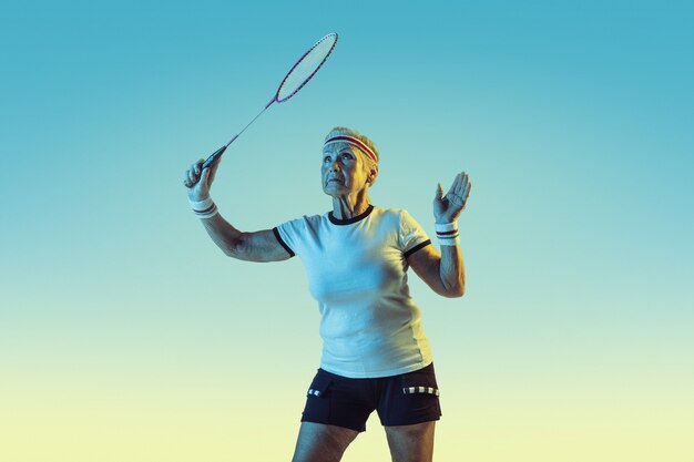 Senior femme jouant au badminton en vêtements de sport sur gradient en néon