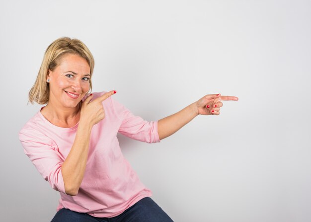 Senior femme souriante en chemisier rose pointant sur le côté