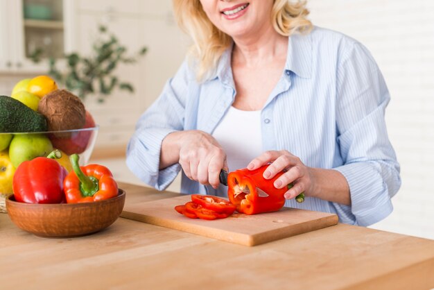 Senior femme souriante coupe le poivron rouge avec un couteau