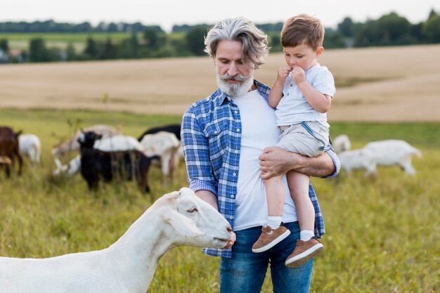 Senior holding petit garçon en jouant avec des chèvres