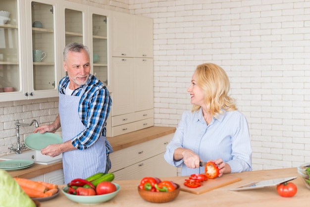 Senior homme aidant sa femme à couper le poivron avec un couteau dans la cuisine