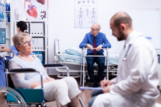 Senior homme assis sur un lit d'hôpital avec déambulateur en attente de consultation