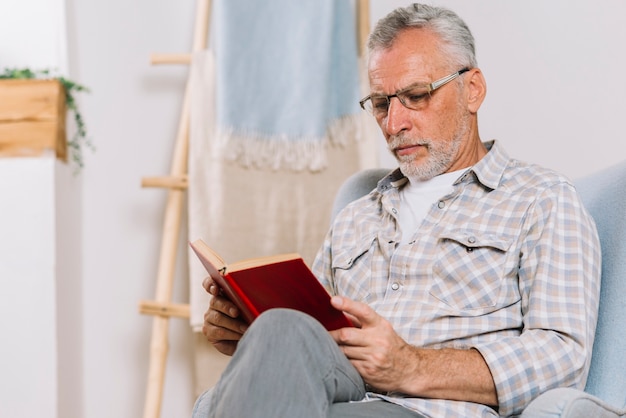 Senior homme assis sur un livre de lecture de fauteuil