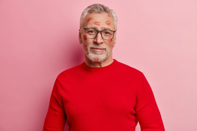 Senior homme ayant des taches de rouge à lèvres sur le visage et portant un pull rouge
