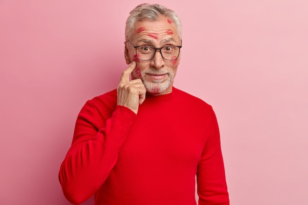 Senior homme ayant des taches de rouge à lèvres sur le visage et portant un pull rouge