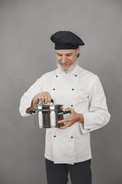 Senior homme avec casserole en métal. Chef dans un chapeau noir.