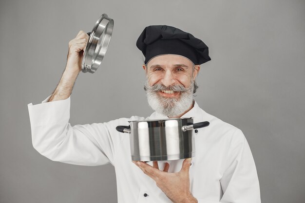 Senior homme avec casserole en métal. Chef dans un chapeau noir.