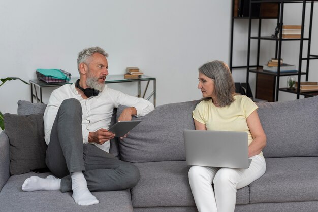 Senior homme et femme à la maison sur le canapé à l'aide d'un ordinateur portable et d'une tablette