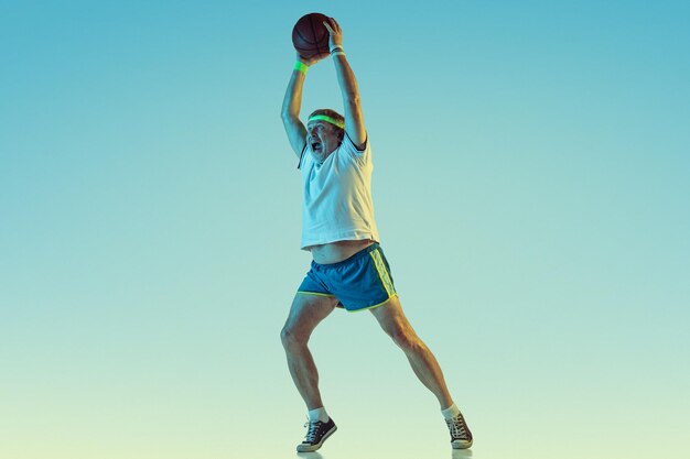 Senior homme jouant au basket sur fond dégradé en néon. Le mannequin caucasien en grande forme reste actif, sportif.