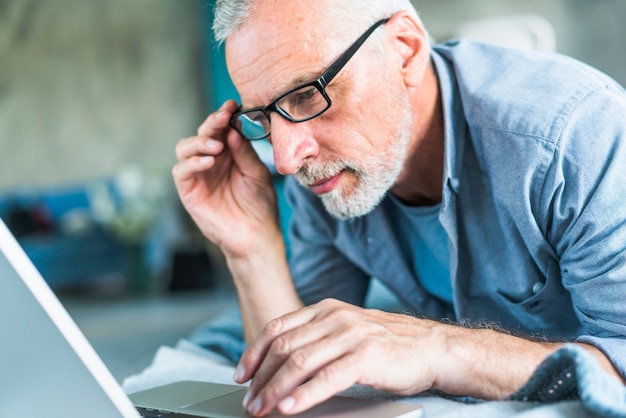 Senior homme avec la main sur les lunettes en regardant ordinateur portable