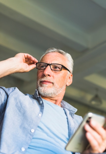 Senior homme avec la main sur les lunettes, tenant le téléphone portable