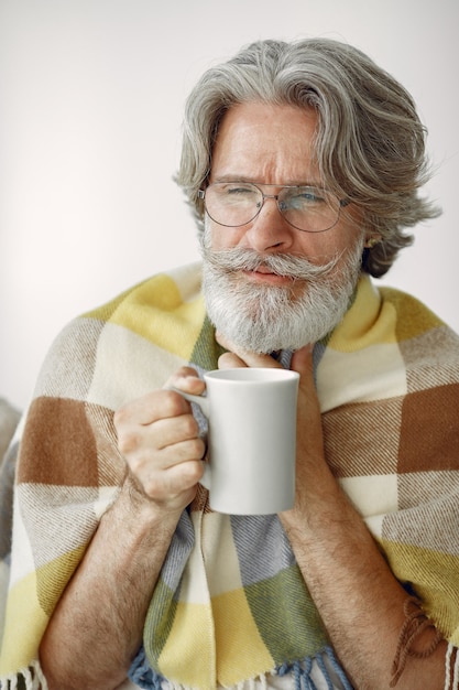 Senior homme seul assis sur un canapé. Homme malade recouvert de plaid. Grangfather avec une tasse de thé.