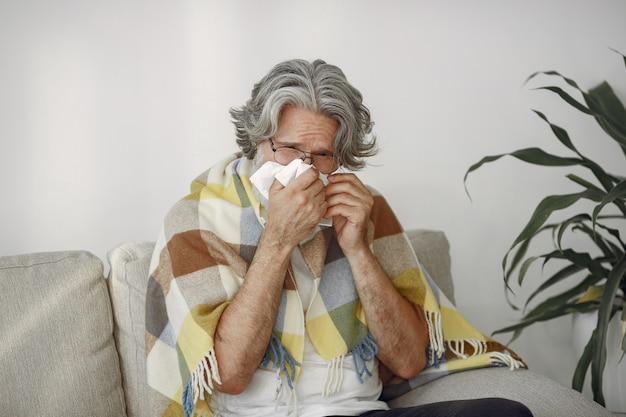 Senior homme seul assis sur un canapé. Homme malade recouvert de plaid.