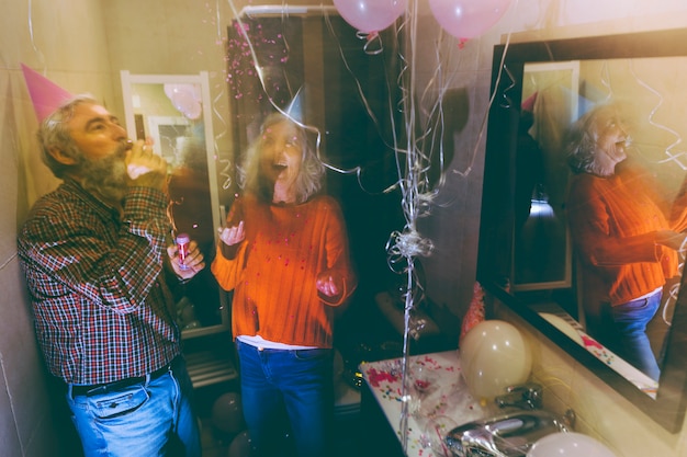 Photo gratuite senior homme soufflant la corne du parti et femme jetant des confettis dans les airs pour anniversaire