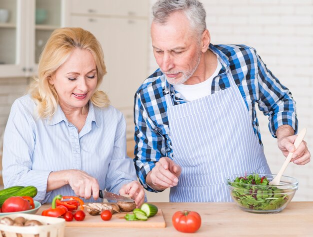 Senior homme souriant aide sa femme à préparer une salade dans la cuisine