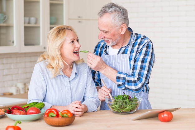 Photo gratuite senior homme souriant donnant une salade verte à sa femme dans la cuisine