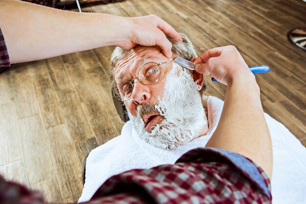 Senior homme visite coiffeur en salon de coiffure.