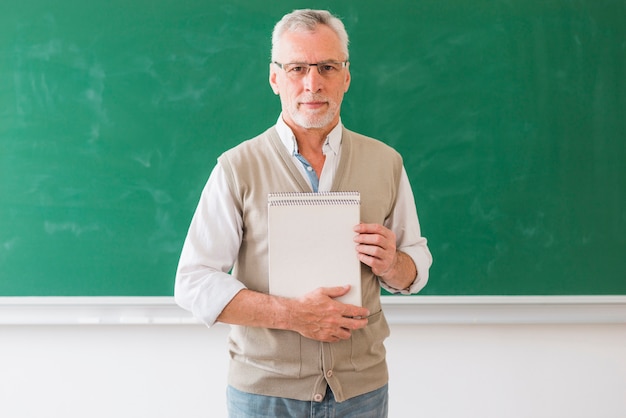 Senior mâle, professeur, tenue, cahier, debout, contre, tableau noir