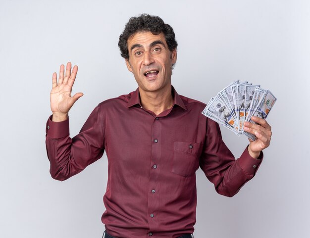 Senior man in purple shirt holding cash looking at camera heureux et confiant montrant le numéro cinq