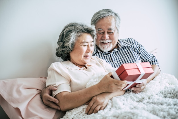Senior mari souriant faisant une boîte-cadeau surprise à sa femme dans la chambre