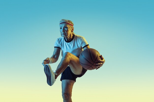 Senior woman in sportwear jouant au basketball sur gradient