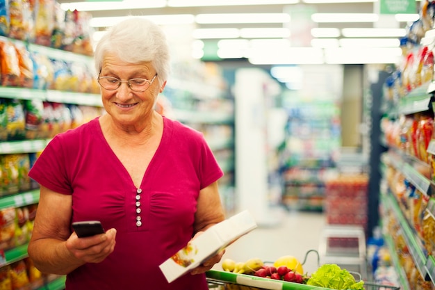 Senior woman textos sur téléphone mobile au supermarché