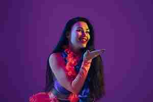 Photo gratuite sensuel, baiser. modèle brune hawaïenne sur mur violet en néon. belles femmes en vêtements traditionnels souriant et s'amusant. vacances lumineuses, couleurs de célébration, festival.