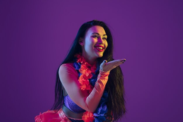 Sensuel, baiser. Modèle brune hawaïenne sur mur violet en néon. Belles femmes en vêtements traditionnels souriant et s'amusant. Vacances lumineuses, couleurs de célébration, festival.