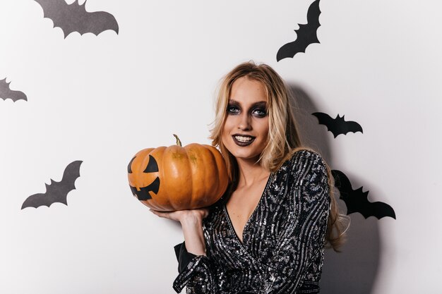 Sensuelle jeune femme avec maquillage noir tenant la citrouille. fille spectaculaire se préparant pour la fête d'halloween.