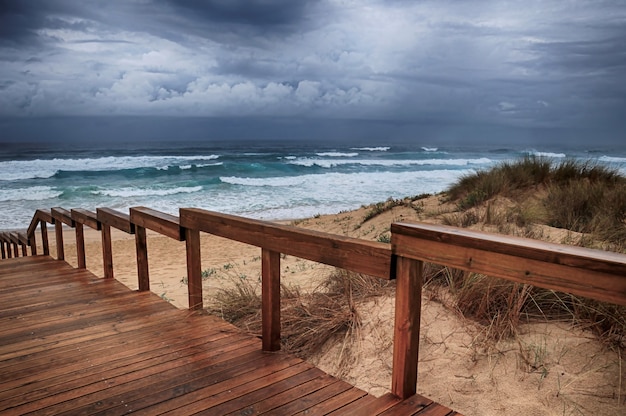 Sentier en bois sur la plage par les vagues de l'océan à couper le souffle sous le ciel nuageux