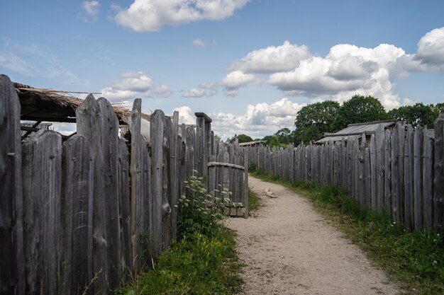 Sentier entouré de clôtures en bois et de verdure sous un ciel nuageux pendant la journée