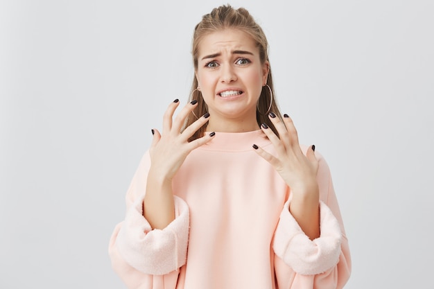 Sentiment et émotions humains. Insatisfaite belle fille caucasienne aux cheveux blonds vêtue d'un sweat rose montrant son dégoût et son aversion pour quelque chose qu'elle n'aime pas, fronçant les sourcils.