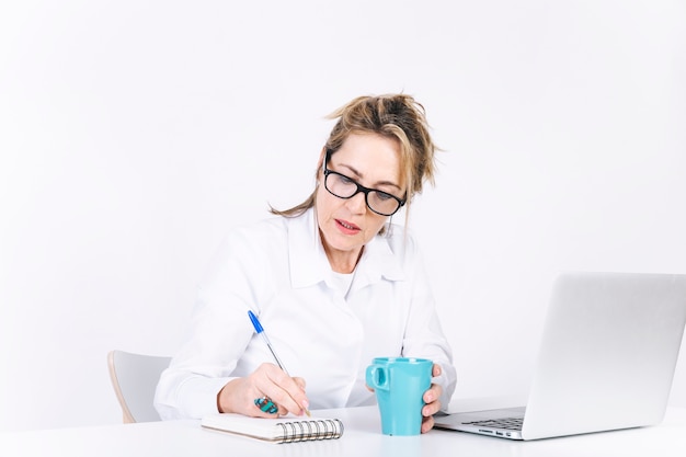 Sérieuse femme écrivant dans un cahier près d&#39;un ordinateur portable