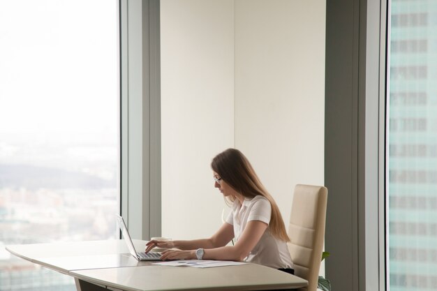 Sérieuse femme occupée travaillant sur un ordinateur portable à l&#39;intérieur du bureau, fond