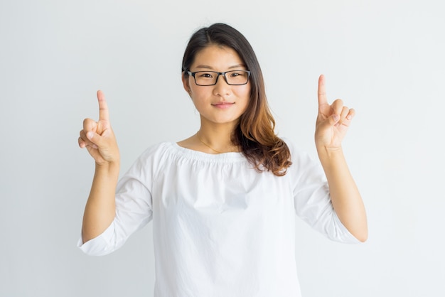 Sérieuse fille asiatique intelligente avec des cheveux mis en évidence pointant vers le haut avec les doigts.