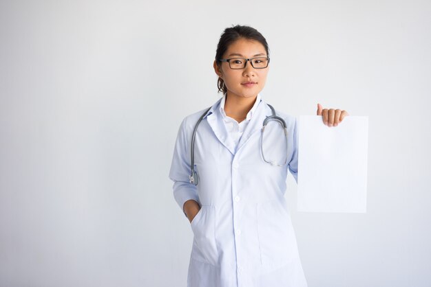 Sérieuse jeune femme asiatique montrant une feuille de papier vierge.