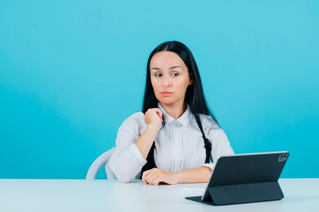 Sérieusement, la blogueuse pose devant la caméra de la tablette en tenant la main sur l'épaule sur fond bleu