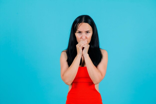 Sérieusement, la fille regarde la caméra en tenant les mains sur la bouche sur fond bleu