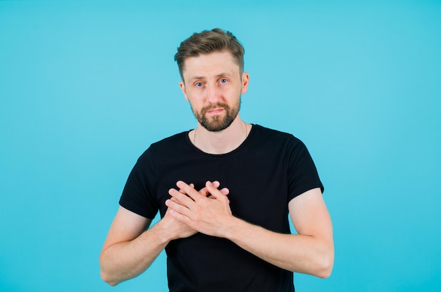 Sérieusement, L'homme Regarde La Caméra En Tenant Les Mains Sur Le Cœur Sur Fond Bleu