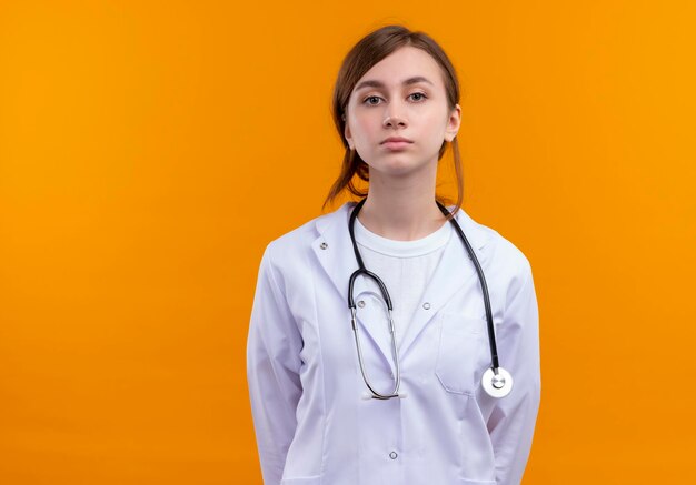 Sérieusement à la jeune femme médecin portant une robe médicale et un stéthoscope à la recherche sur l'espace orange isolé avec copie espace