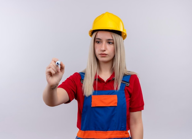 Photo gratuite sérieusement à la jeune fille blonde ingénieur constructeur en écriture uniforme avec un marqueur sur un espace blanc isolé