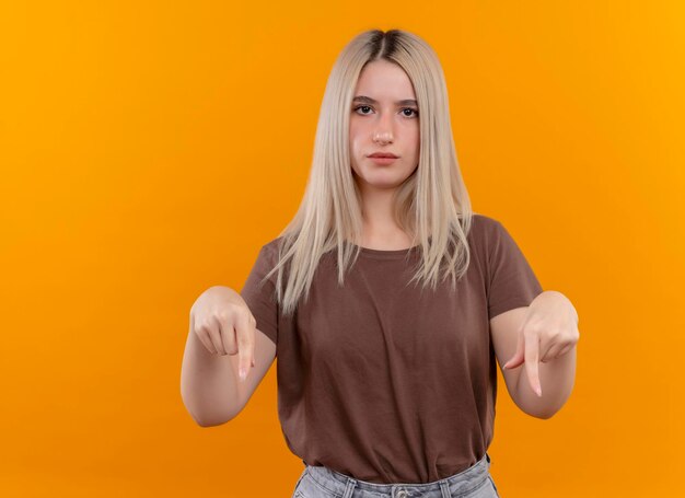 Sérieusement à la jeune fille blonde pointant vers le bas sur l'espace orange isolé avec copie espace