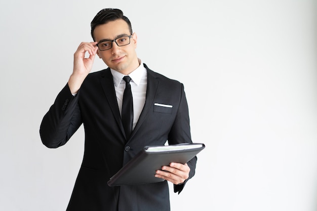 Sérieux beau jeune homme d&#39;affaires ajustant des lunettes et tenant le dossier.