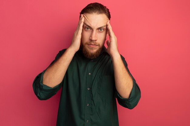 Sérieux bel homme blond met les mains sur les tempes isolées sur le mur rose