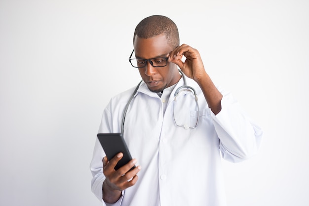 Sérieux homme médecin noir lisant des nouvelles sur smartphone.