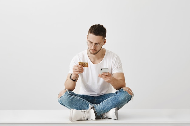 Sérieux jeune homme avec des lunettes posant avec son téléphone et sa carte