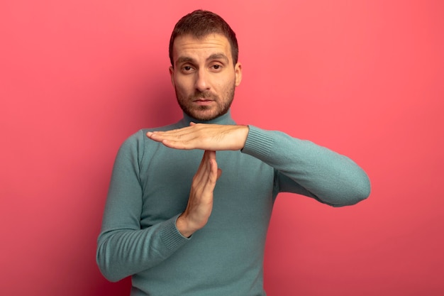 Photo gratuite sérieux jeune homme regardant avant faisant le geste de délai d'attente isolé sur mur rose