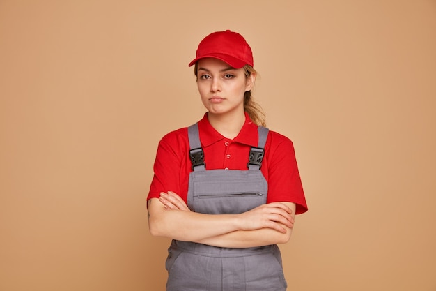 Sérieux jeune ouvrier féminin portant l'uniforme et le chapeau debout avec une posture fermée