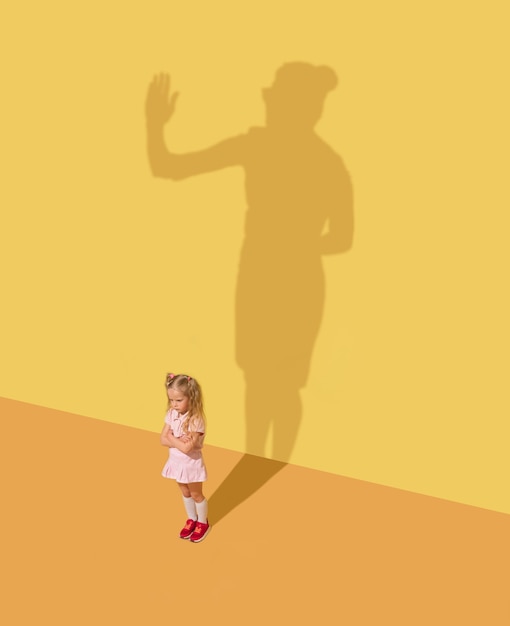 Photo gratuite sérieux et juste. concept d'enfance et de rêve. image conceptuelle avec enfant et ombre sur le mur jaune du studio. la petite fille veut devenir femme d'affaires, femme de bureau et se bâtir une carrière.