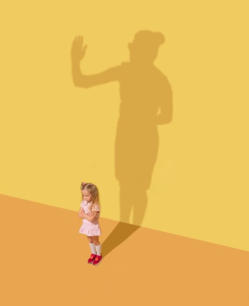 Sérieux et juste. Concept d'enfance et de rêve. Image conceptuelle avec enfant et ombre sur le mur jaune du studio. La petite fille veut devenir femme d'affaires, femme de bureau et se bâtir une carrière.